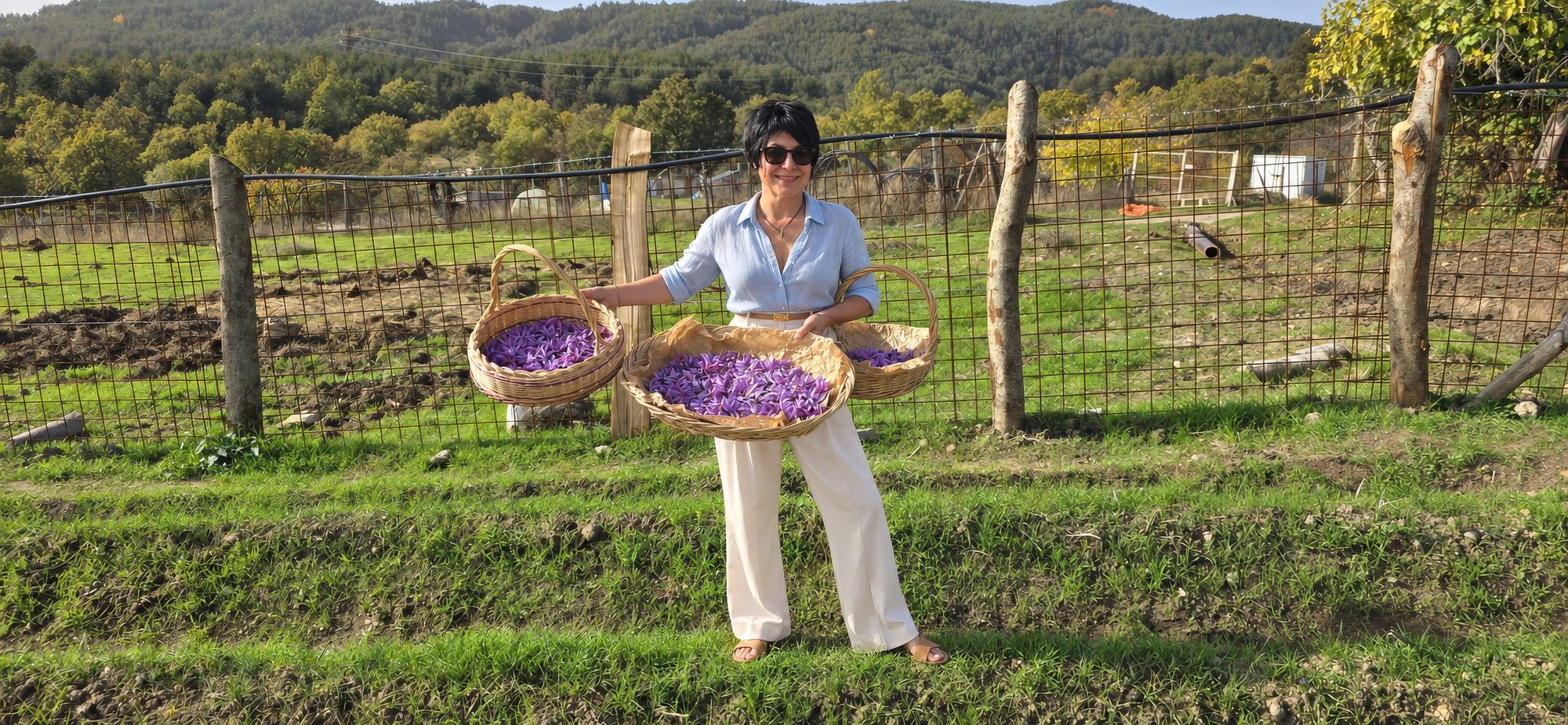 Anna Rita con tre cesti di fiori di zafferano davanti alla recinzione della tenuta